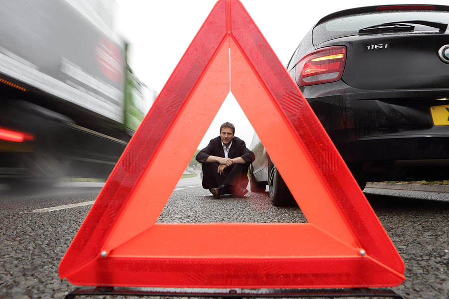 Man viewed through warning triangle, broken car Photograph by Peter Cade