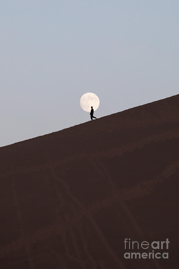 Man walking in front of the moon in the desert Photograph by Matteo Colombo