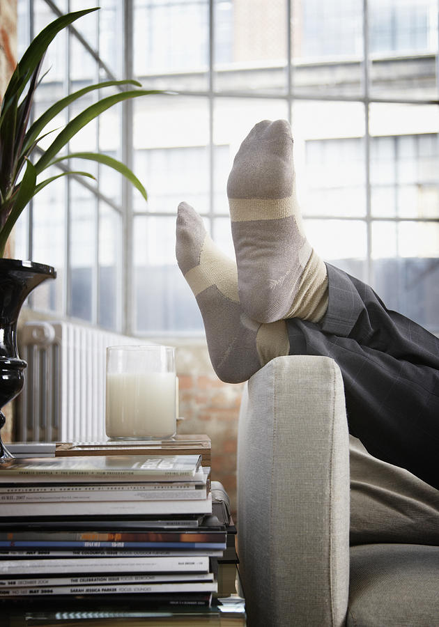 Mans feet up on arm of couch in modern home Photograph by Paul Bradbury
