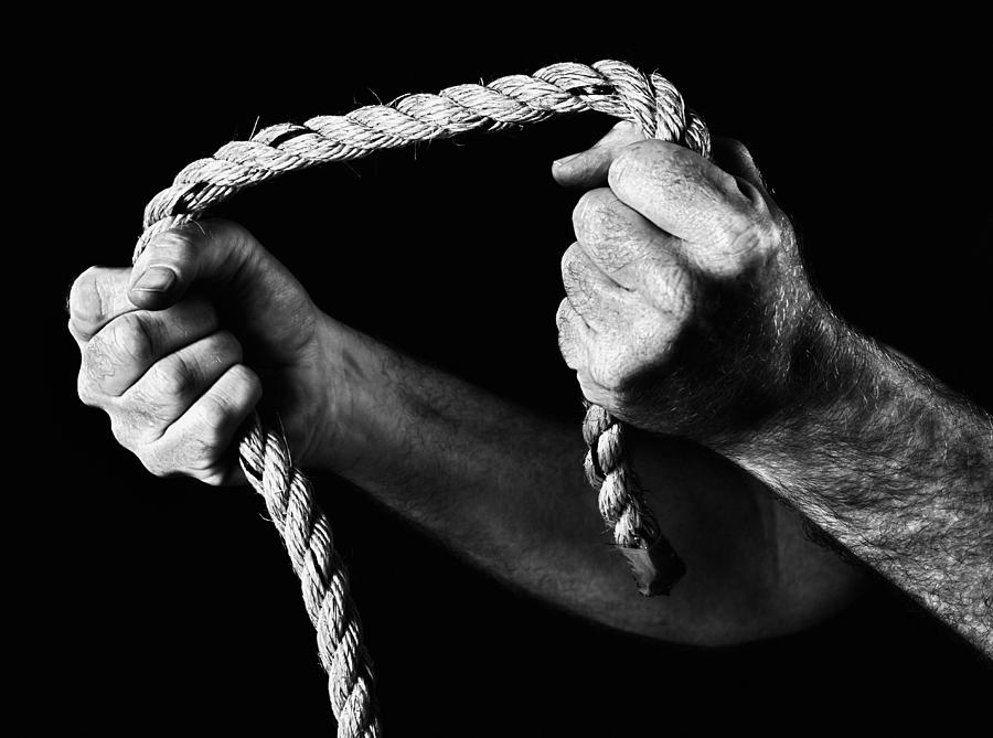 Masculine hands grip rope, pulling apart. Black and white. Photograph by RapidEye