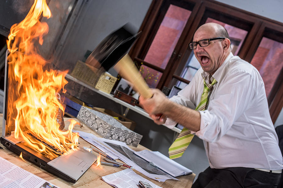 Mature adult businessman smashing laptop on fire with hammer Photograph by Vm