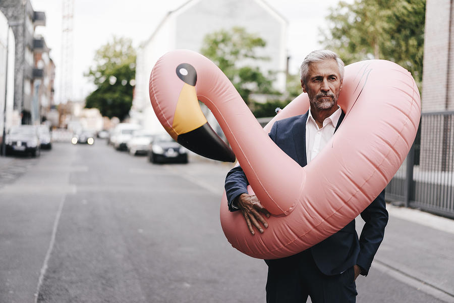 Mature businessman on the street with inflatable flamingo Photograph by Westend61
