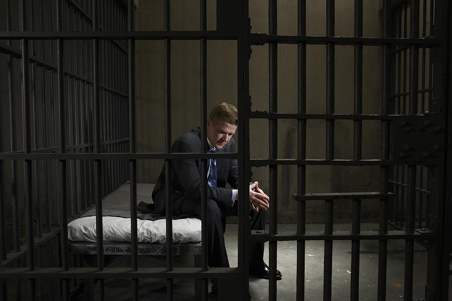 Mature businessman sitting on bed in prison cell Photograph by Darrin Klimek