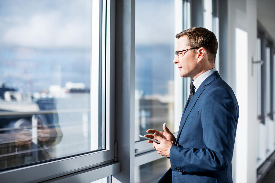 Mature businessman standing by window in office Photograph by Alvarez