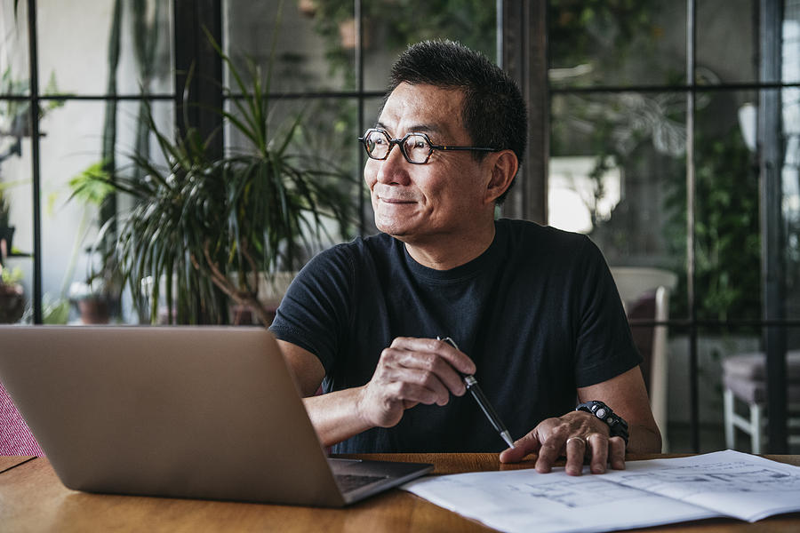 Mature Chinese man using laptop at home Photograph by JohnnyGreig
