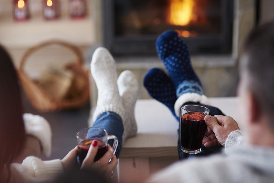 Mature couple with hot drinks in living room at the fireplace Photograph by Westend61