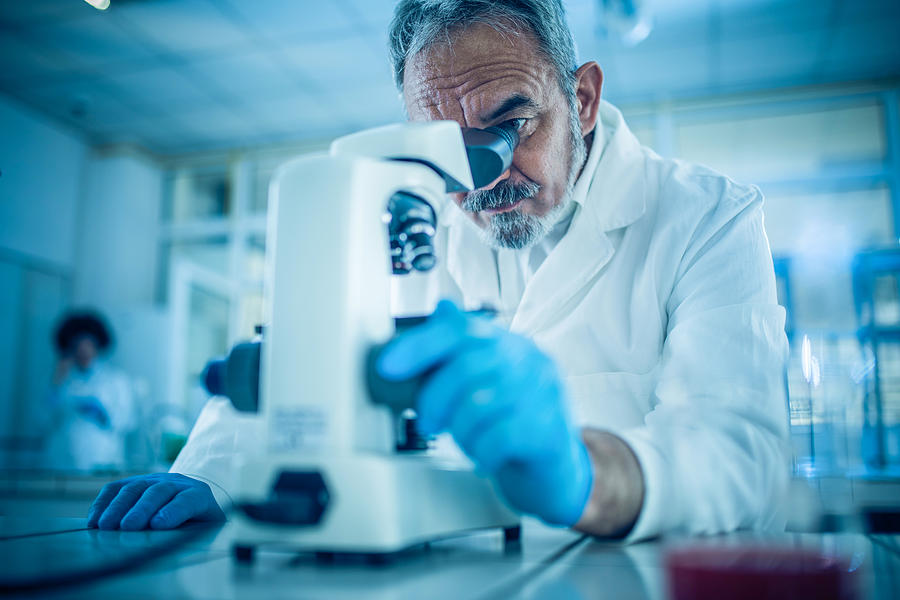 Mature forensic scientist looking through microscope while working on research in a laboratory Photograph by Skynesher