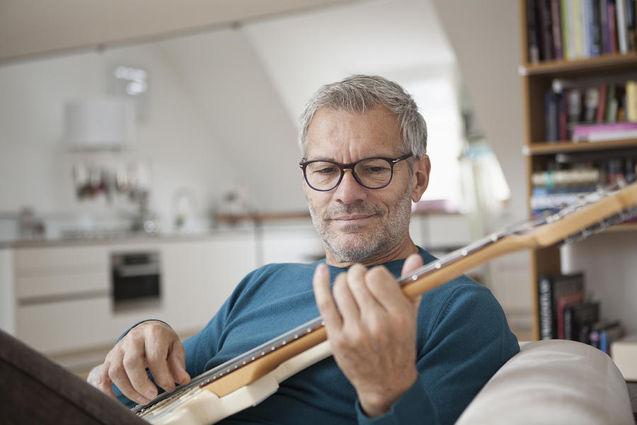 Mature man at home playing guitar Photograph by Westend61