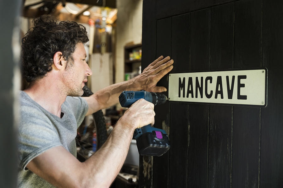 Mature man fixing mancave sign on wooden door Photograph by Portra