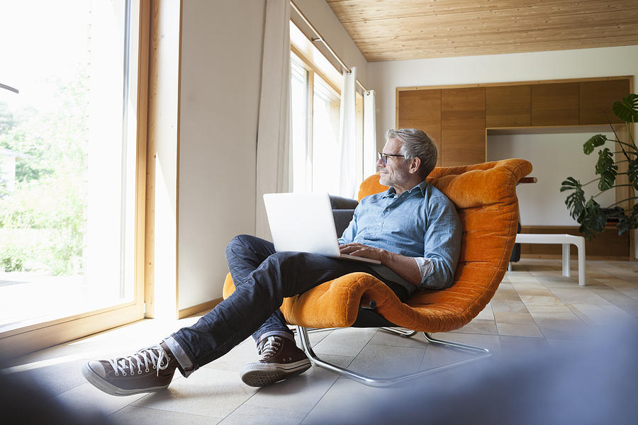 Mature man using laptop in armchair Photograph by Westend61