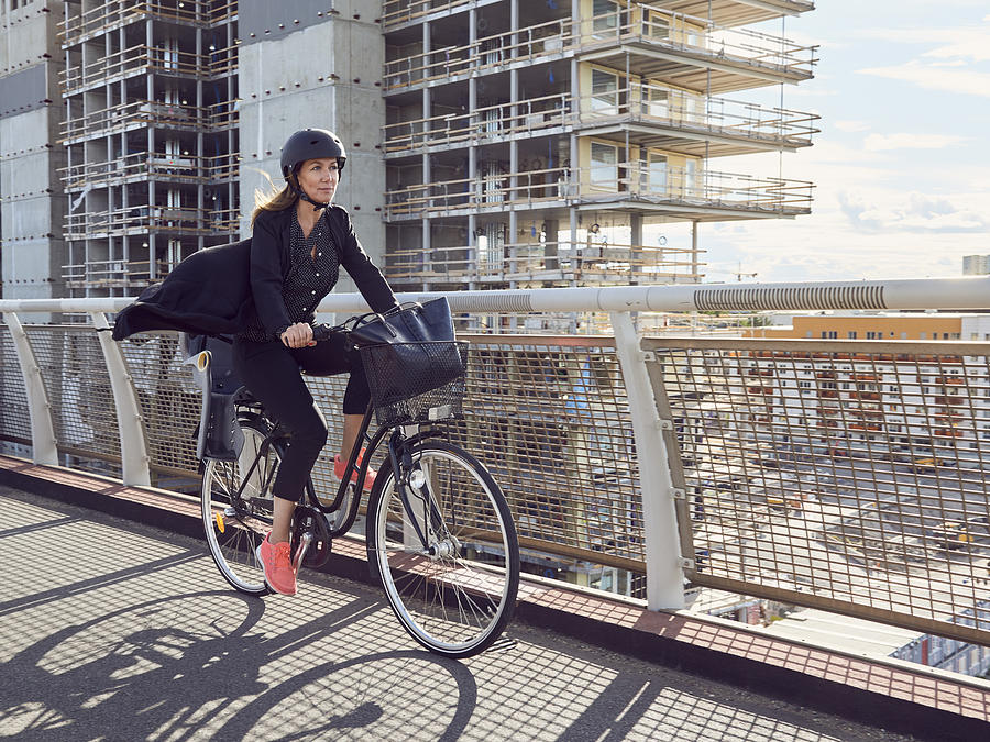 Mature woman cycling on footbridge against building Photograph by Maskot