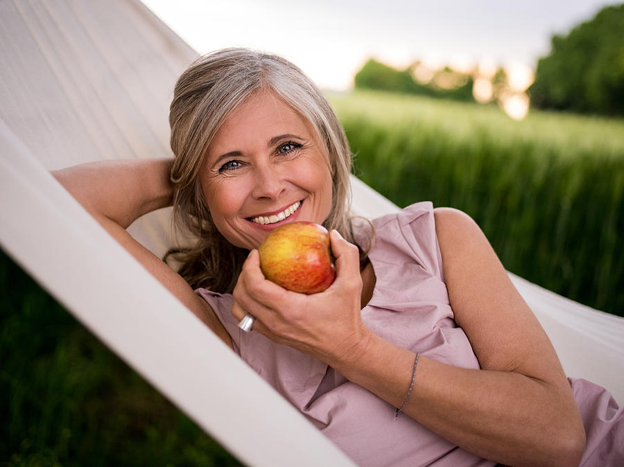 Mature woman eating a fresh apple while relaxing outdoors Photograph by Wundervisuals