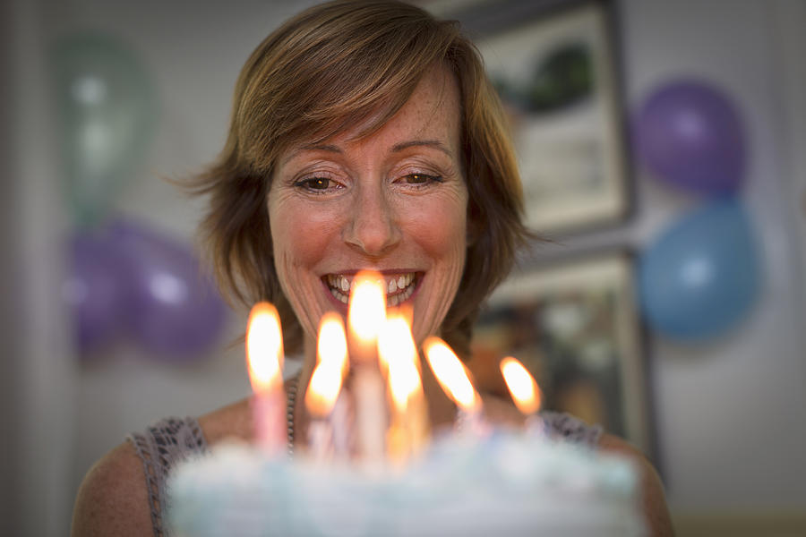 Mature woman holding birthday cake with candles Photograph by Steve Prezant