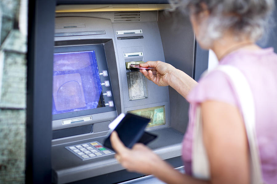 Mature woman inserting credit card into local french cash machine Photograph by Jag Images