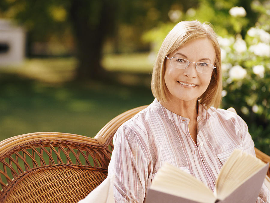 Mature Woman Sitting in a Garden Reading a Book Photograph by Flying Colours Ltd