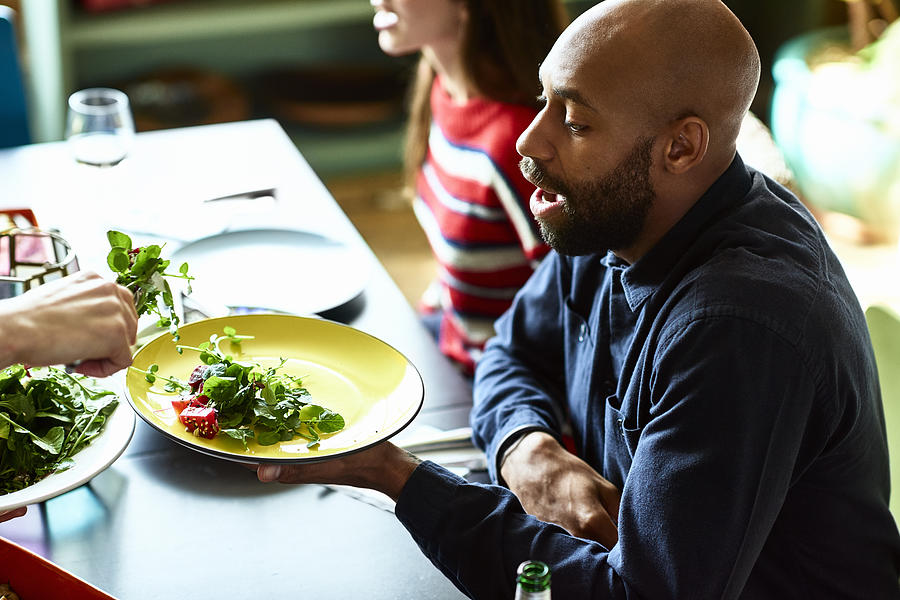 Mid adult man at dinner party holding plate and being served salad Photograph by 10000 Hours