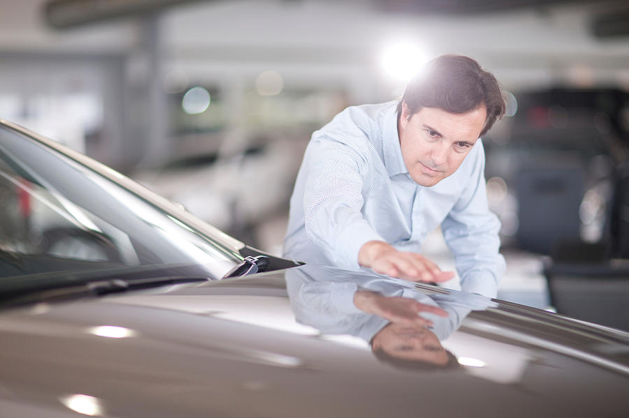 Mid adult man looking at car bonnet in showroom Photograph by Zero Creatives