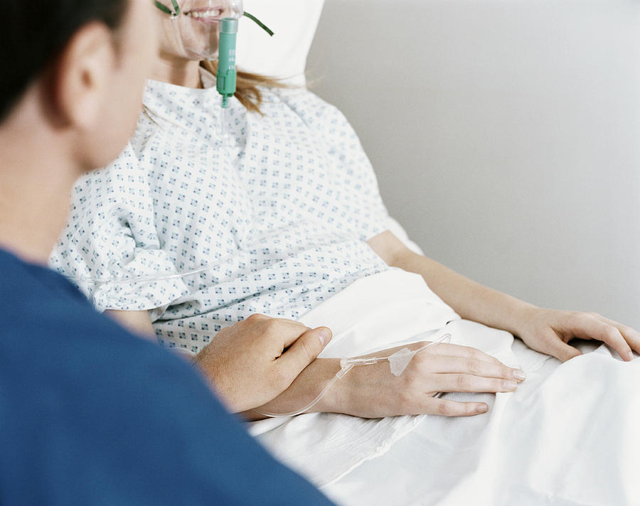 Mid Section of a Woman Lying in a Hospital Bed With a Ventilator and Intravenous Drip, a Man Holding Her Hand Photograph by Janie Airey