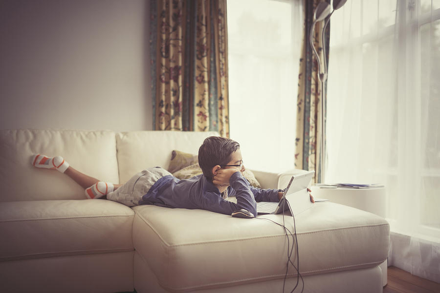 Mixed race boy using digital tablet on sofa Photograph by Donald Iain Smith