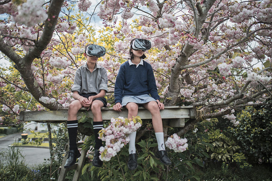 Mixed Race brother and sister sitting in tree wearing virtual reality goggles Photograph by Donald Iain Smith