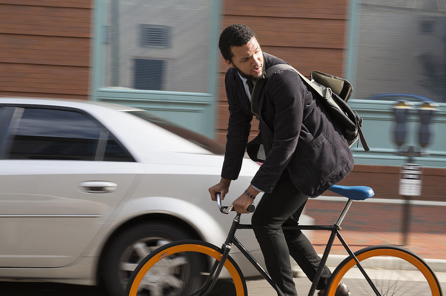 Mixed race businessman riding bicycle on city street Photograph by Roberto Westbrook