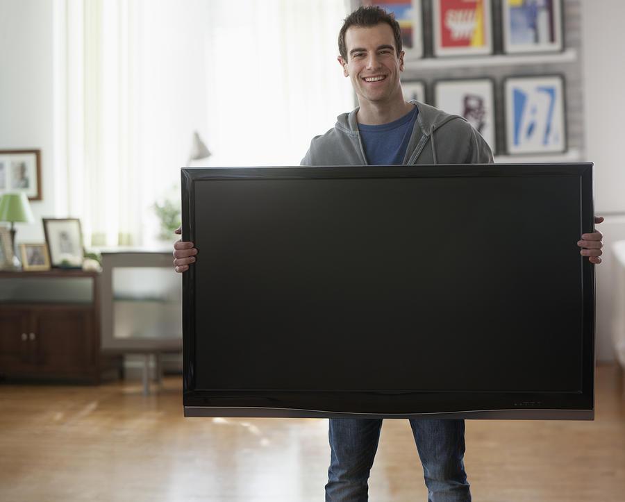 Mixed race man holding big screen television Photograph by Jose Luis Pelaez Inc