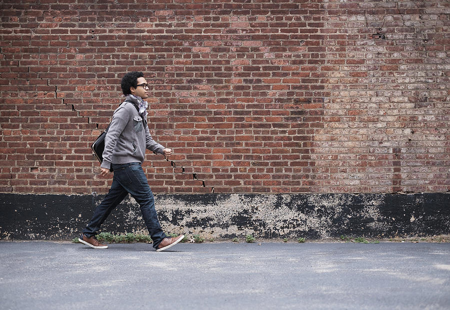 Mixed race man walking near brick wall Photograph by JGI/Tom Grill