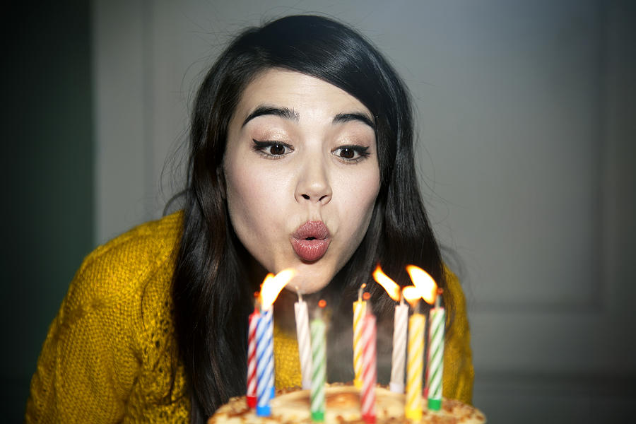Mixed race woman blowing out birthday candles Photograph by Ezra Bailey