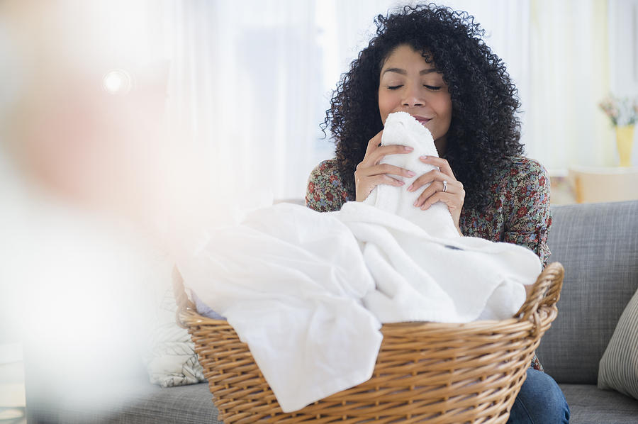 Mixed race woman smelling clean towels in laundry Photograph by JGI/Jamie Grill
