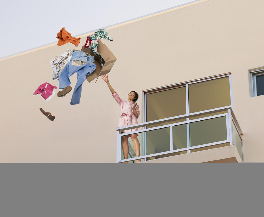 Mixed race woman throwing clothes off balcony Photograph by John M Lund Photography Inc