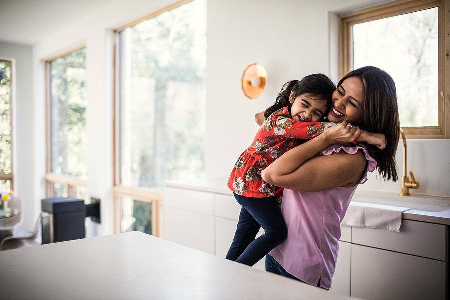 Mother and daughter embracing in kitchen Photograph by MoMo Productions