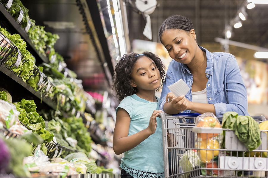 Mother and daughter grocery shop together using list Photograph by SDI Productions