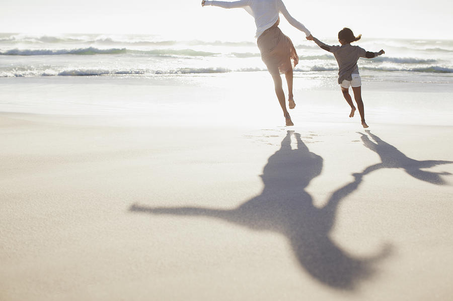 Mother and daughter holding hands and running on sunny beach Photograph by Sam Edwards