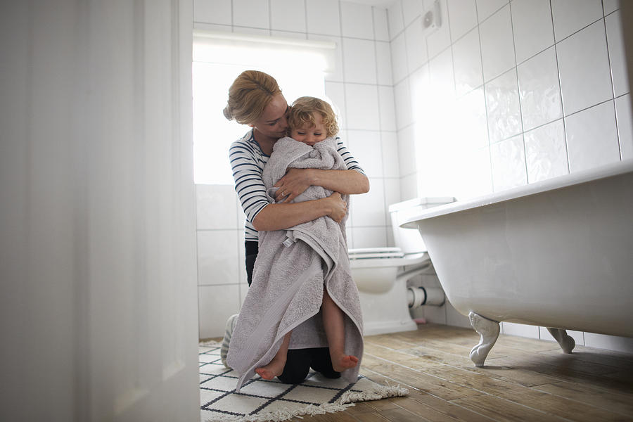 Mother and daughter in bathroom, mother wrapping daughter in bath towel, hugging her Photograph by Peter Muller