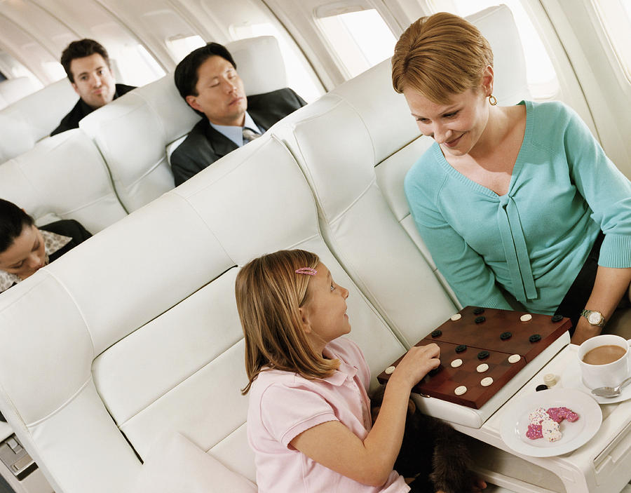 Mother and Daughter Playing Draughts, and Passengers in the Background in an Aircraft Cabin Interior Photograph by Digital Vision.