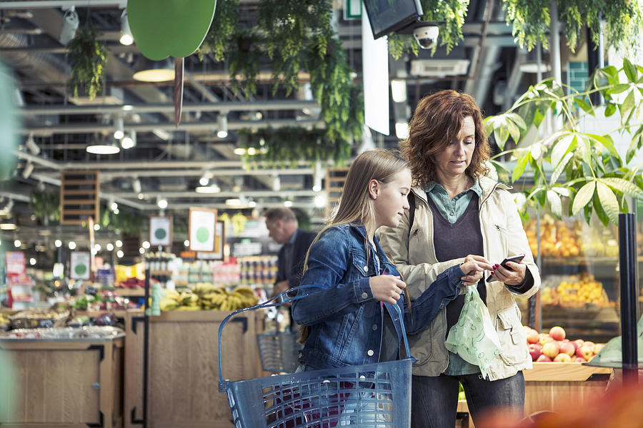 Mother and daughter using smart phone in organic foodstore Photograph by Kentaroo Tryman