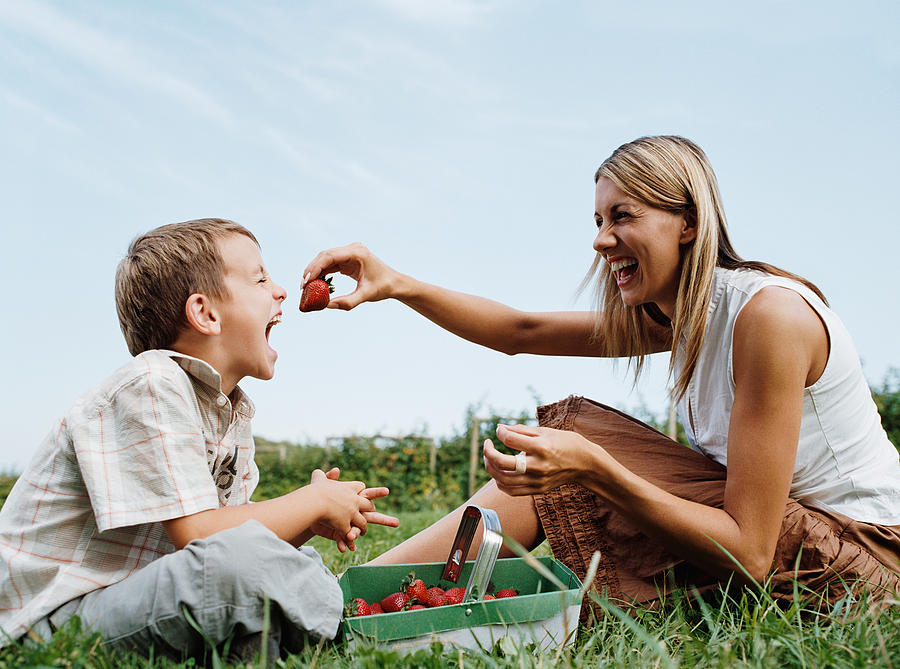 Mother feeding strawberry to son Photograph by Image Source