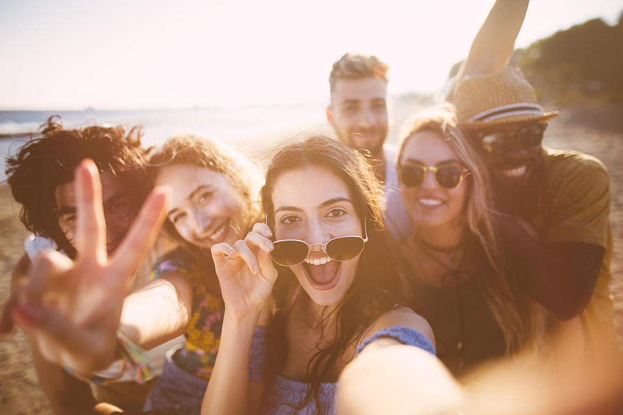 Multi-ethnic friends taking selfies at the beach on summer holidays Photograph by Wundervisuals