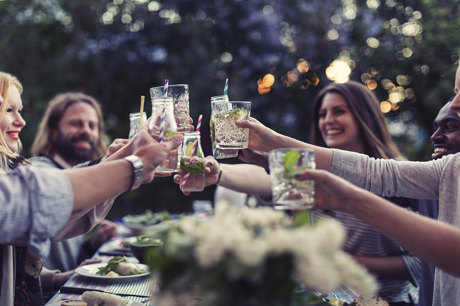 Multi-ethnic friends toasting mojito glasses at dinner table in yard Photograph by Maskot