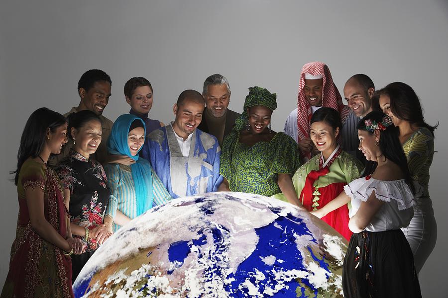 Multi-ethnic people in traditional dress looking at globe Photograph by Jon Feingersh Photography Inc