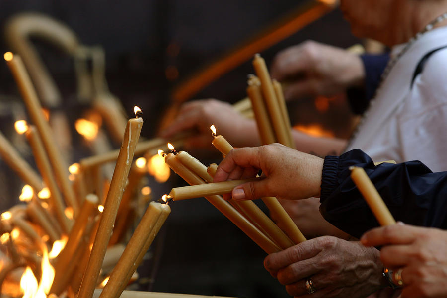 Multiple pairs of hands lighting gold candles Photograph by LuisPortugal