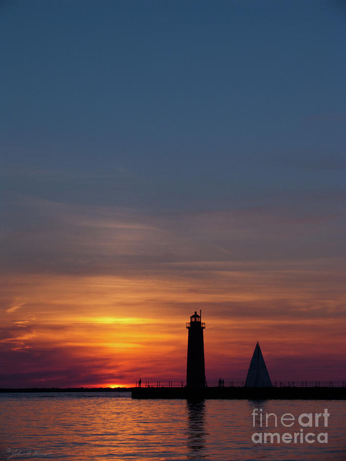 Muskegon lighthouse Silhouetted at sunset with a sailboat in the Photograph by John Harmon