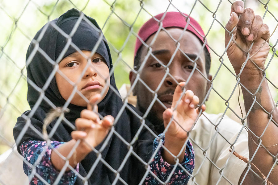 Muslim mid adult black man holding his daughter looking through a fence Photograph by Juanmonino