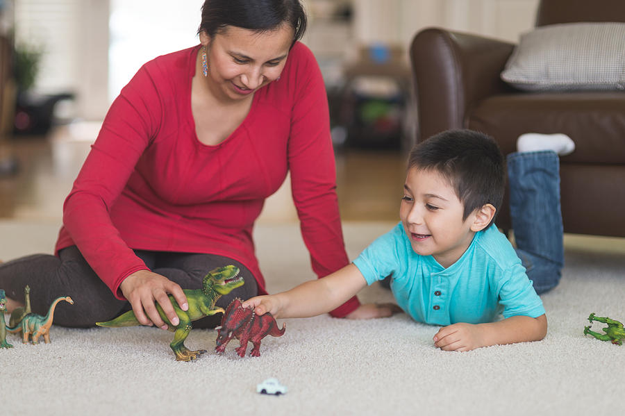 Native American mom plays with her son and toy dinosaurs on the living room floor Photograph by FatCamera