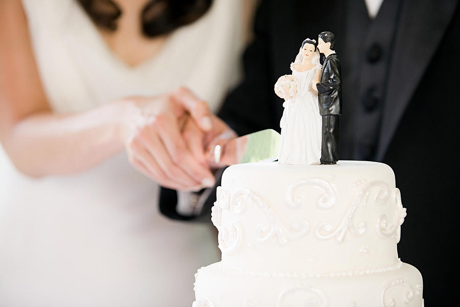 Newlyweds cutting wedding cake Photograph by Image Source