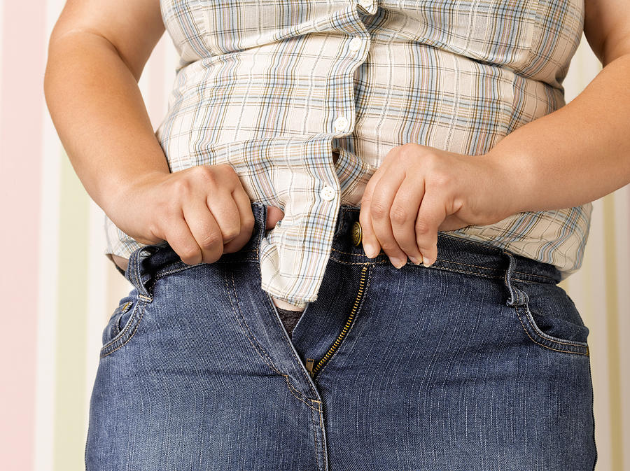Obese teenager doing up jeans Photograph by Peter Dazeley
