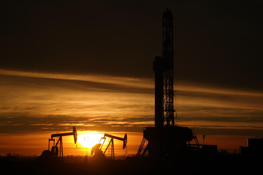 Oil rig and two pumpjacks in the sunset Photograph by Jeff Swan
