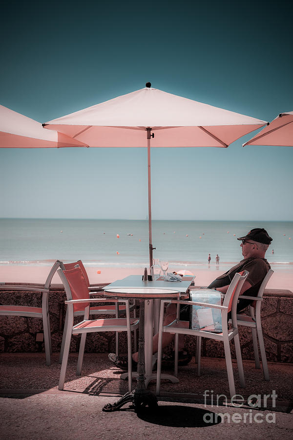 One man sitting under umbrella at cafe table by beach. Photograph by Peter Noyce