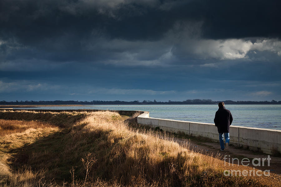 One Man Walking Alone By Sea Wall In Sunshine On Dramatic Stormy Photograph by Peter Noyce