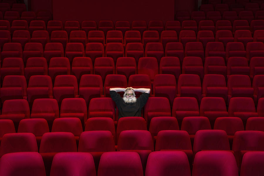 One man with white beard sits in Empty cinema or theatre with comfortable red seats Photograph by Pidjoe